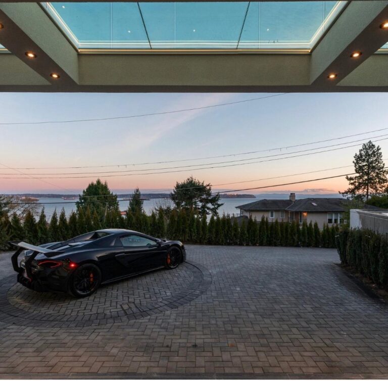 Covered porte-cochère with a glass skylight and pavered driveway overlooking the ocean at sunset at a luxury custom home