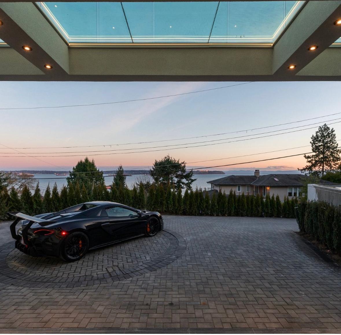 Covered porte-cochère with a glass skylight and pavered driveway overlooking the ocean at sunset at a luxury custom home