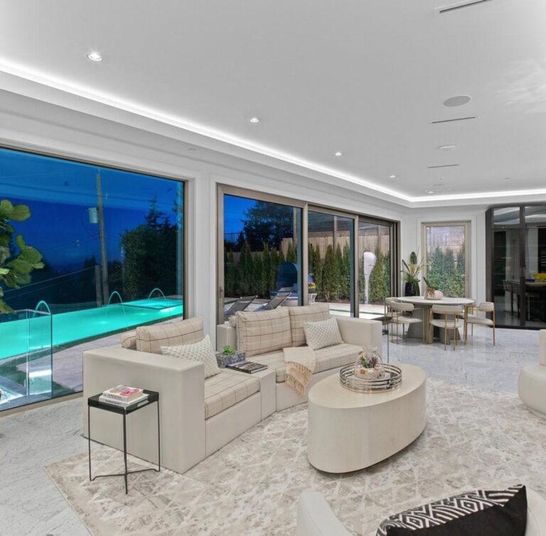 Bright living room with cove lighting and marble floors, with large windows onto a lit infinity-edge pool at dusk
