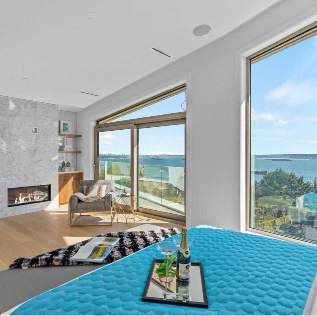 Primary bedroom with a marble-clad linear fireplace and floor-to-ceiling sliding glass doors opening to an ocean-view balcony