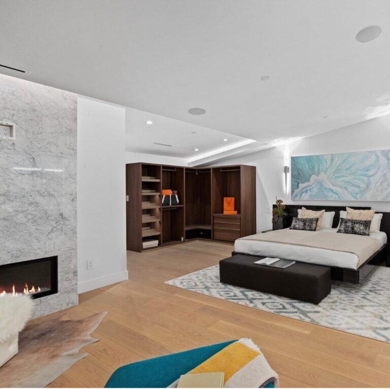 Spacious primary suite with a marble fireplace surround, open walnut walk-in closet and wide-plank oak floors